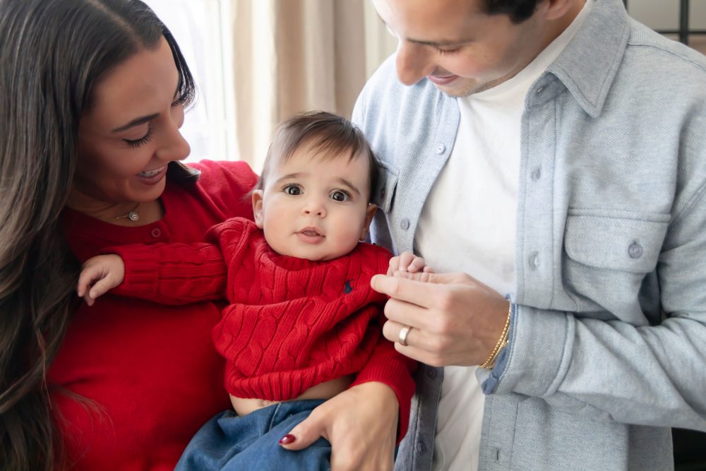 Cleveland in-home family photoshoot with mom, dad, and baby boy featuring natural light lifestyle photography, cozy candid moments, Valentine’s theme with red sweaters and chocolates, and their family dog