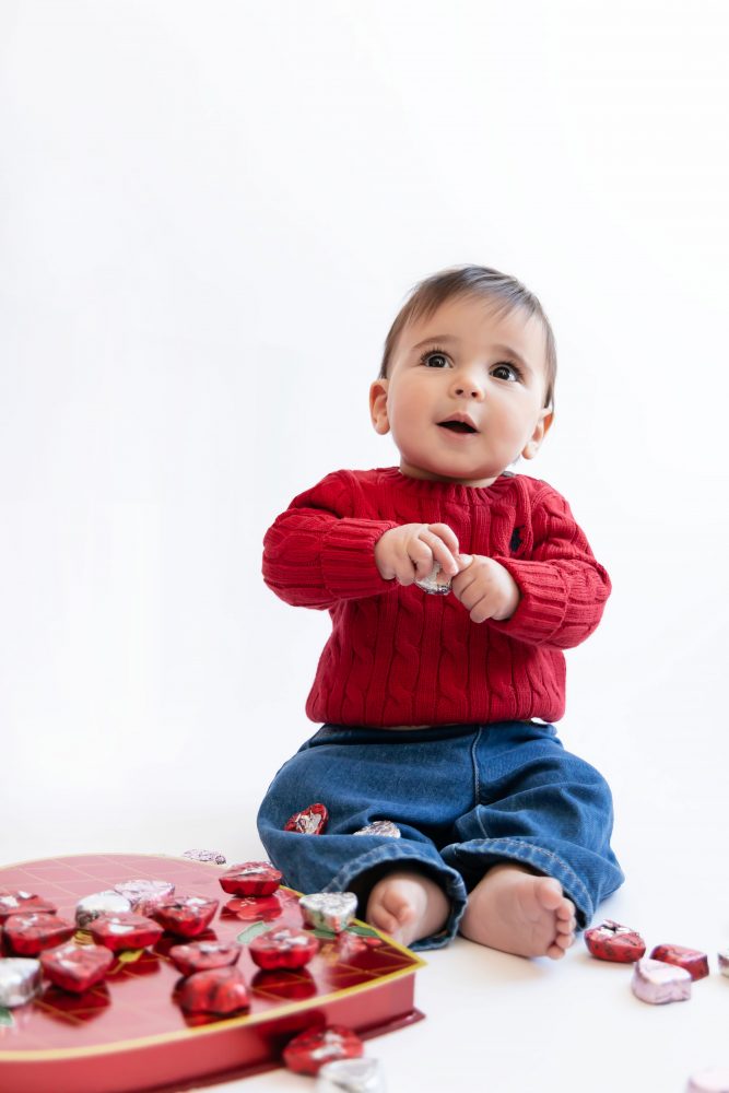 Cleveland in-home family photoshoot with mom, dad, and baby boy featuring natural light lifestyle photography, cozy candid moments, Valentine’s theme with red sweaters and chocolates, and their family dog