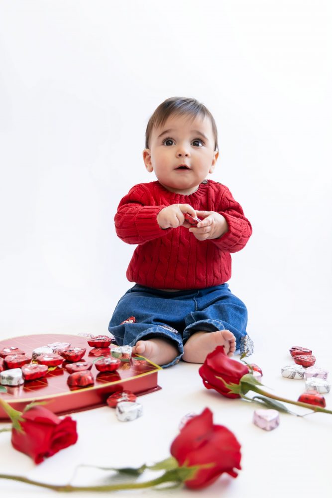 Cleveland in-home family photoshoot with mom, dad, and baby boy featuring natural light lifestyle photography, cozy candid moments, Valentine’s theme with red sweaters and chocolates, and their family dog