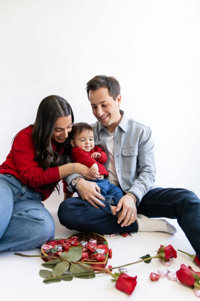 Cleveland in-home family photoshoot with mom, dad, and baby boy featuring natural light lifestyle photography, cozy candid moments, Valentine’s theme with red sweaters and chocolates, and their family dog