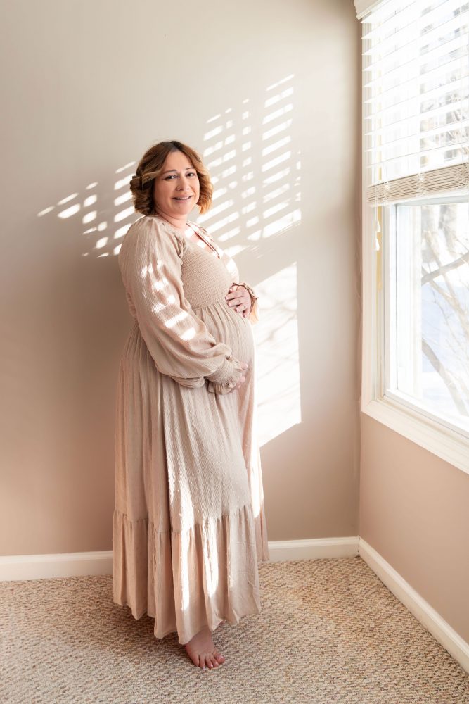 Cleveland maternity photography session of a pregnant mother with her young daughter, captured in soft natural window light by Allison Liffman Photography, highlighting a growing family and sibling connection in a warm, neutral-toned indoor setting