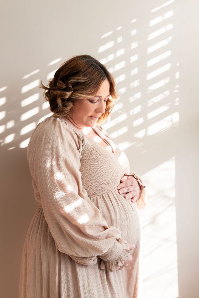 Cleveland maternity photography session of a pregnant mother with her young daughter, captured in soft natural window light by Allison Liffman Photography, highlighting a growing family and sibling connection in a warm, neutral-toned indoor setting