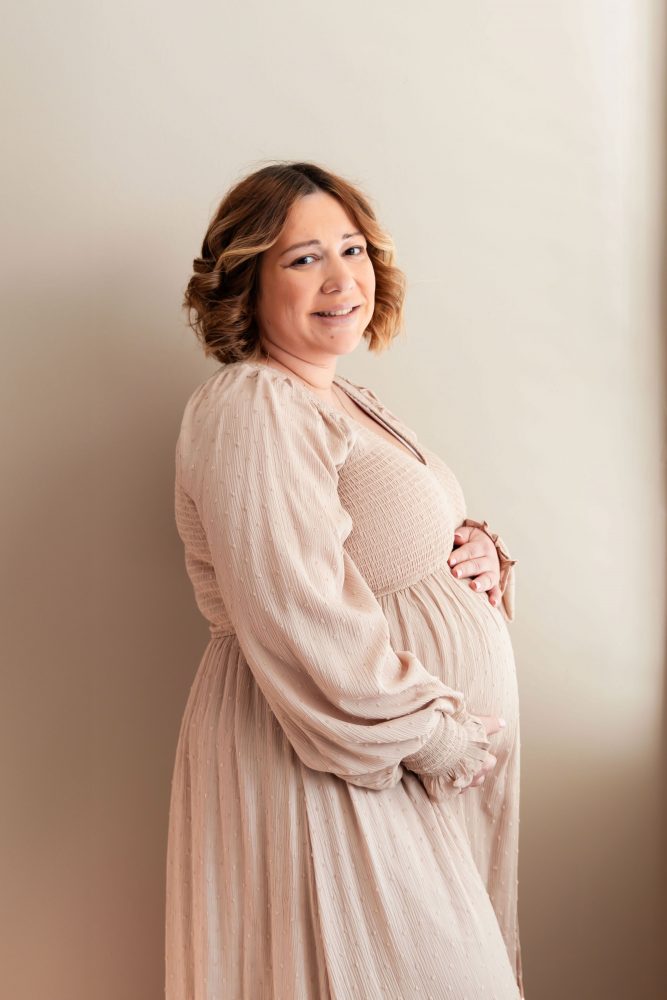Cleveland maternity photography session of a pregnant mother with her young daughter, captured in soft natural window light by Allison Liffman Photography, highlighting a growing family and sibling connection in a warm, neutral-toned indoor setting