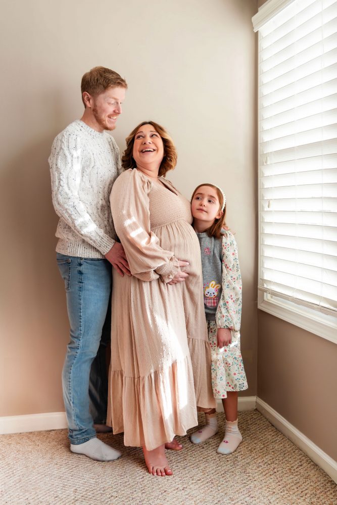 Cleveland maternity photography session of a pregnant mother with her young daughter, captured in soft natural window light by Allison Liffman Photography, highlighting a growing family and sibling connection in a warm, neutral-toned indoor setting