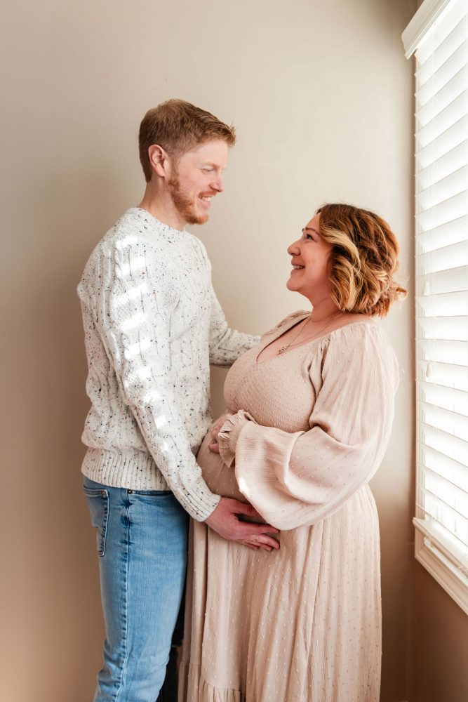 Cleveland maternity photography session of a pregnant mother with her young daughter, captured in soft natural window light by Allison Liffman Photography, highlighting a growing family and sibling connection in a warm, neutral-toned indoor setting