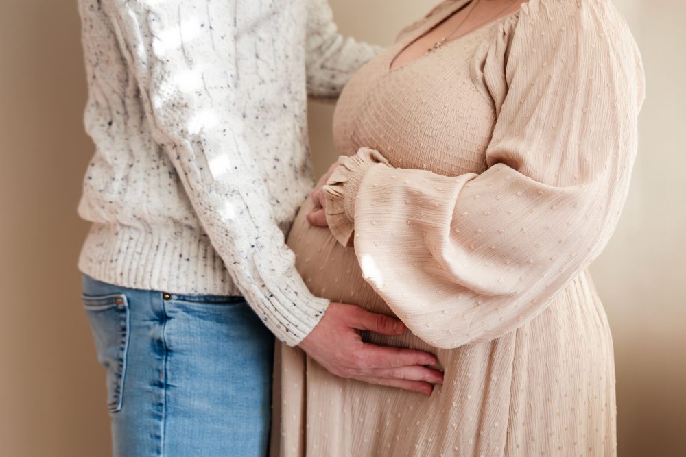 Cleveland maternity photography session of a pregnant mother with her young daughter, captured in soft natural window light by Allison Liffman Photography, highlighting a growing family and sibling connection in a warm, neutral-toned indoor setting