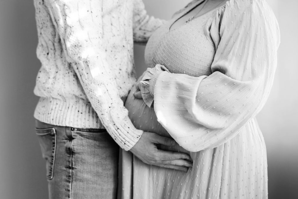Cleveland maternity photography session of a pregnant mother with her young daughter, captured in soft natural window light by Allison Liffman Photography, highlighting a growing family and sibling connection in a warm, neutral-toned indoor setting