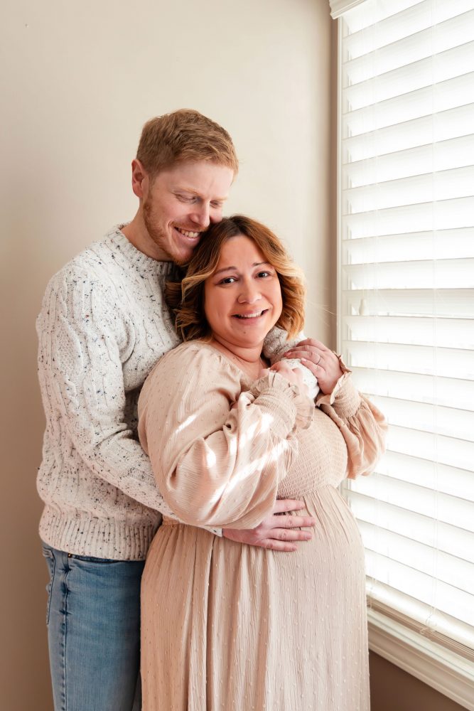 Cleveland maternity photography session of a pregnant mother with her young daughter, captured in soft natural window light by Allison Liffman Photography, highlighting a growing family and sibling connection in a warm, neutral-toned indoor setting
