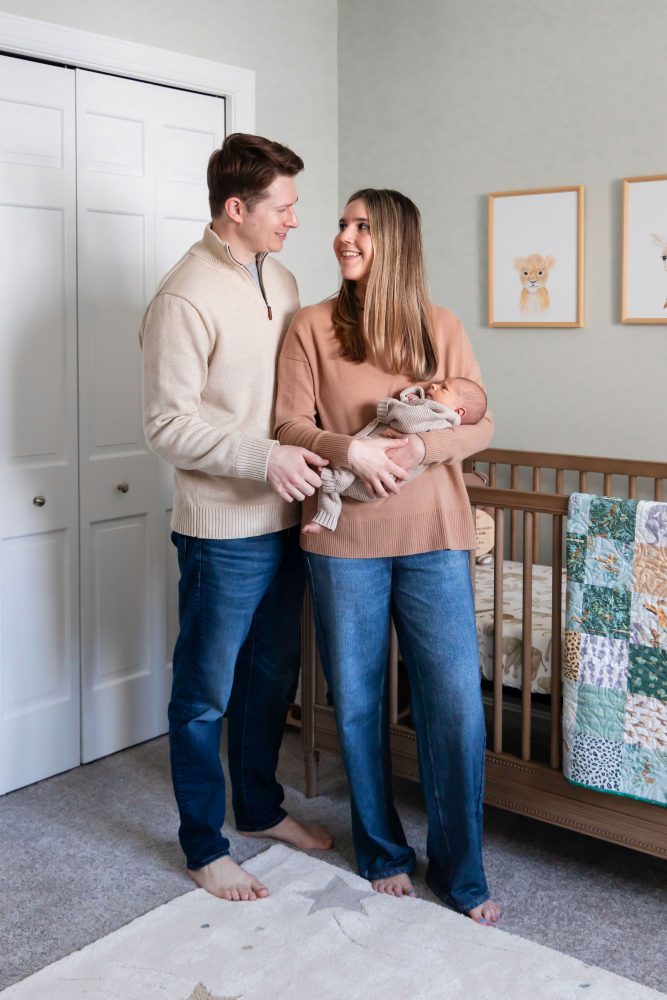 Cleveland newborn and family photographer captures a couple with their newborn baby in a cozy, softly lit nursery, featuring natural light and lifestyle moments in a Cleveland, Ohio home.
