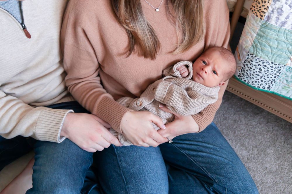 Cleveland newborn and family photographer captures a couple with their newborn baby in a cozy, softly lit nursery, featuring natural light and lifestyle moments in a Cleveland, Ohio home.