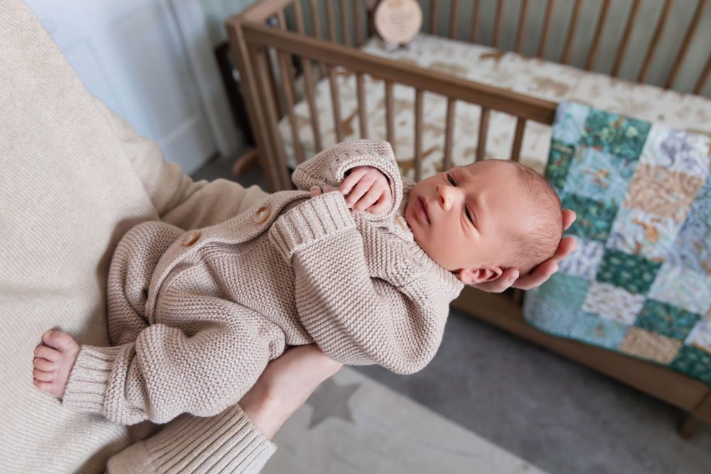 Cleveland newborn and family photographer captures a couple with their newborn baby in a cozy, softly lit nursery, featuring natural light and lifestyle moments in a Cleveland, Ohio home.