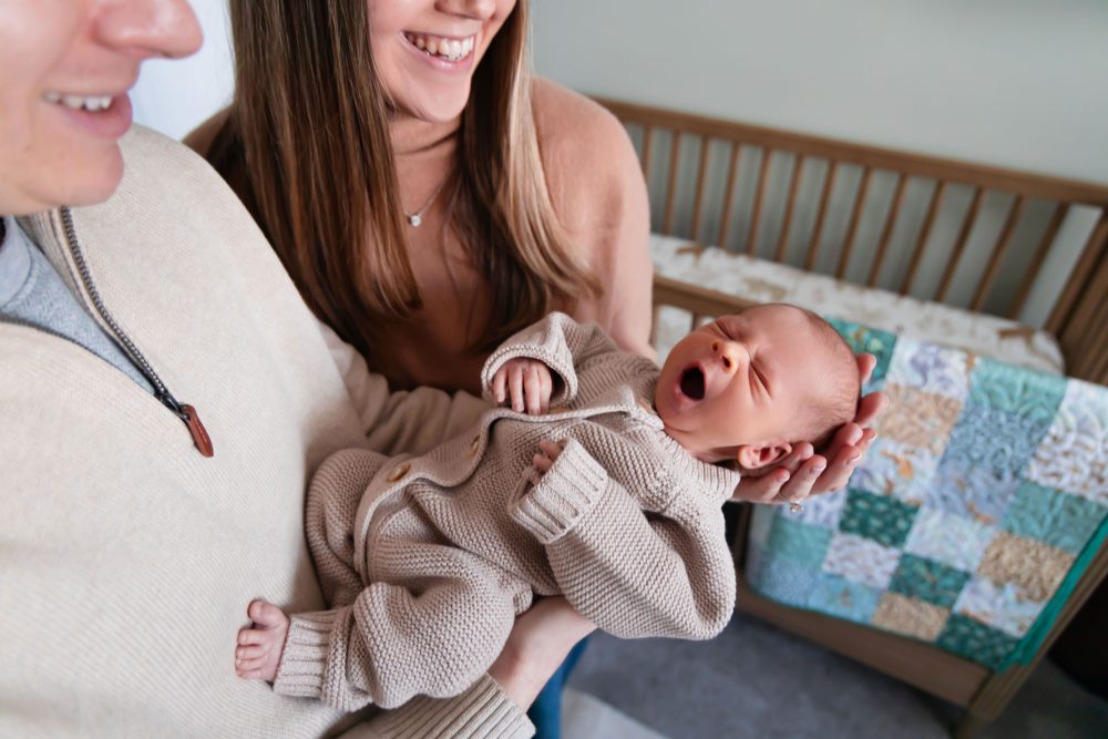 Cleveland newborn and family photographer captures a couple with their newborn baby in a cozy, softly lit nursery, featuring natural light and lifestyle moments in a Cleveland, Ohio home.