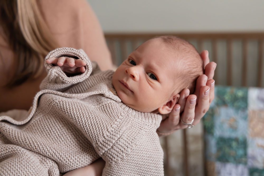 Cleveland newborn and family photographer captures a couple with their newborn baby in a cozy, softly lit nursery, featuring natural light and lifestyle moments in a Cleveland, Ohio home.