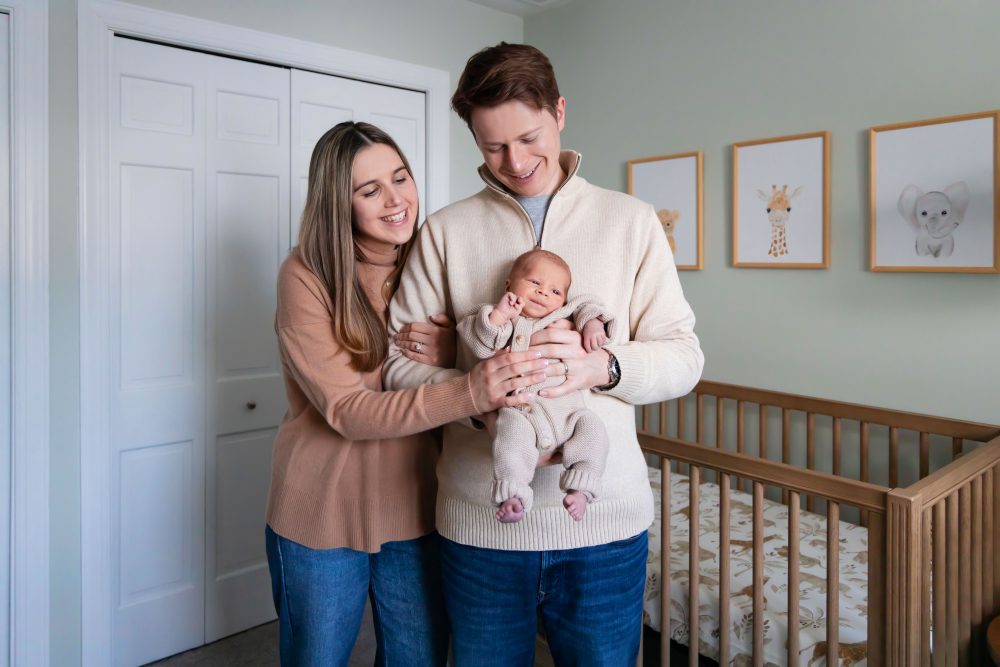 Cleveland newborn and family photographer captures a couple with their newborn baby in a cozy, softly lit nursery, featuring natural light and lifestyle moments in a Cleveland, Ohio home.