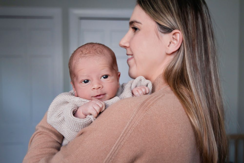 Cleveland newborn and family photographer captures a couple with their newborn baby in a cozy, softly lit nursery, featuring natural light and lifestyle moments in a Cleveland, Ohio home.