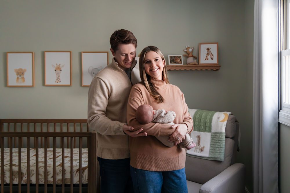 Cleveland newborn and family photographer captures a couple with their newborn baby in a cozy, softly lit nursery, featuring natural light and lifestyle moments in a Cleveland, Ohio home.