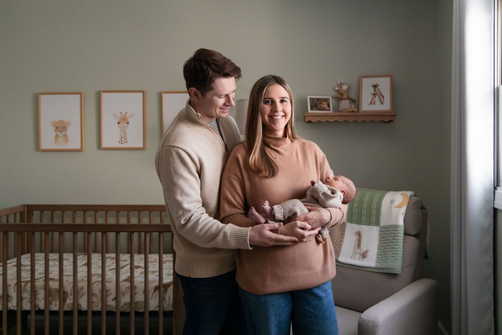 Cleveland newborn and family photographer captures a couple with their newborn baby in a cozy, softly lit nursery, featuring natural light and lifestyle moments in a Cleveland, Ohio home.