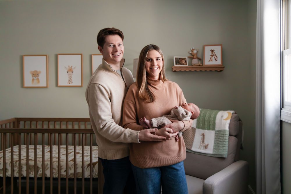 Cleveland newborn and family photographer captures a couple with their newborn baby in a cozy, softly lit nursery, featuring natural light and lifestyle moments in a Cleveland, Ohio home.