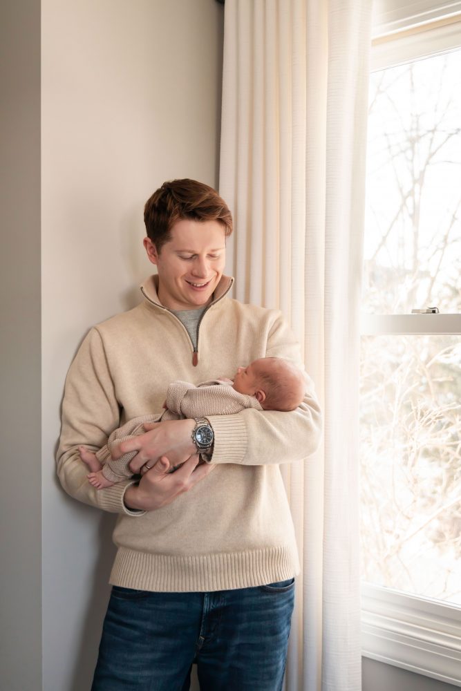 Cleveland newborn and family photographer captures a couple with their newborn baby in a cozy, softly lit nursery, featuring natural light and lifestyle moments in a Cleveland, Ohio home.