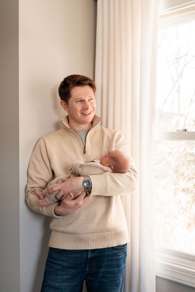 Cleveland newborn and family photographer captures a couple with their newborn baby in a cozy, softly lit nursery, featuring natural light and lifestyle moments in a Cleveland, Ohio home.