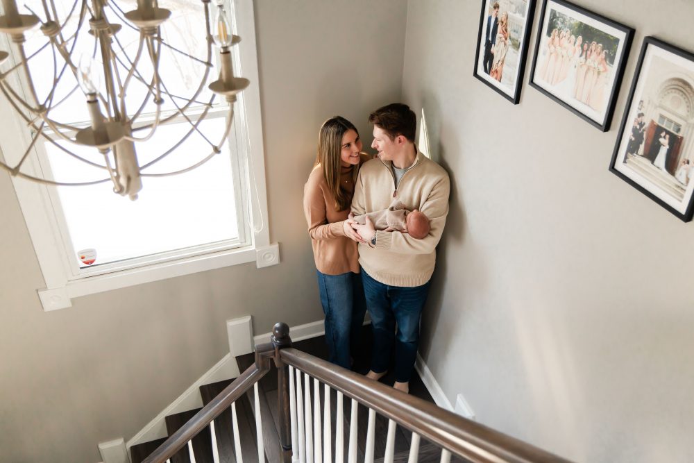 Cleveland newborn and family photographer captures a couple with their newborn baby in a cozy, softly lit nursery, featuring natural light and lifestyle moments in a Cleveland, Ohio home.