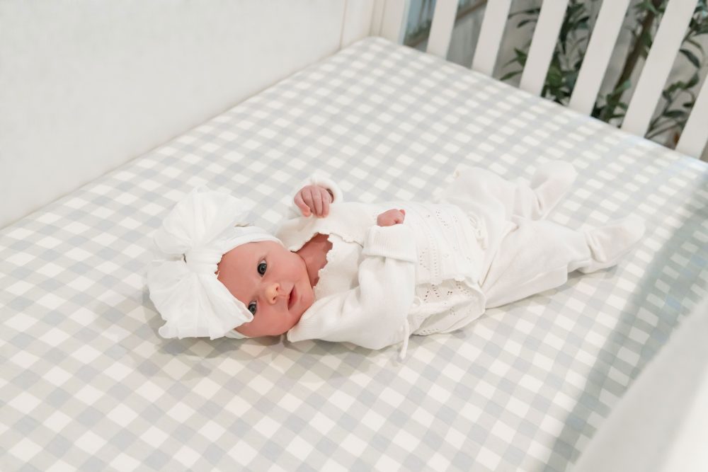 Lifestyle family portrait on a bed featuring newborn baby in the foreground with parents and toddler smiling softly in the background during a cozy in-home newborn session.