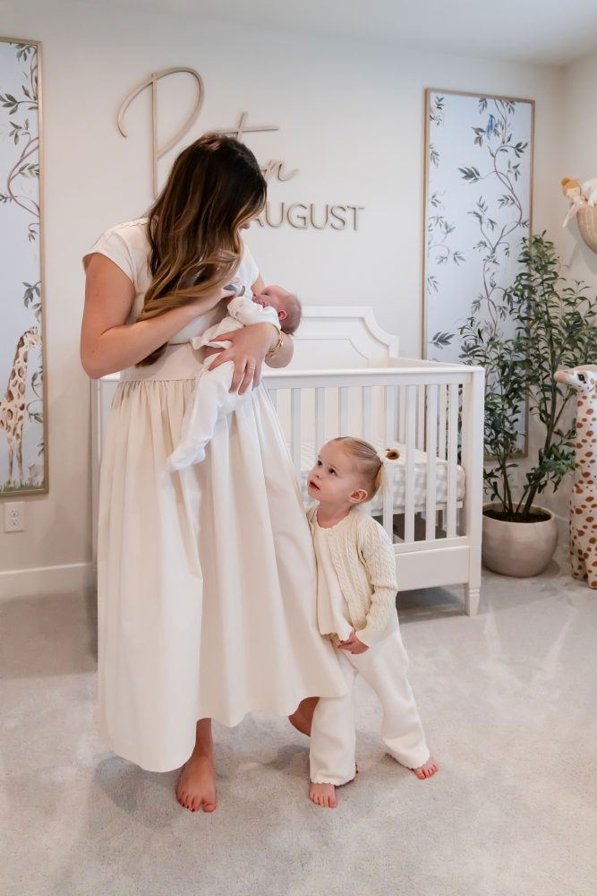 Mother and children standing together in a neutral-toned nursery, parents holding their newborn son while big sister cuddles with dad during an in-home newborn photography session in Cleveland.