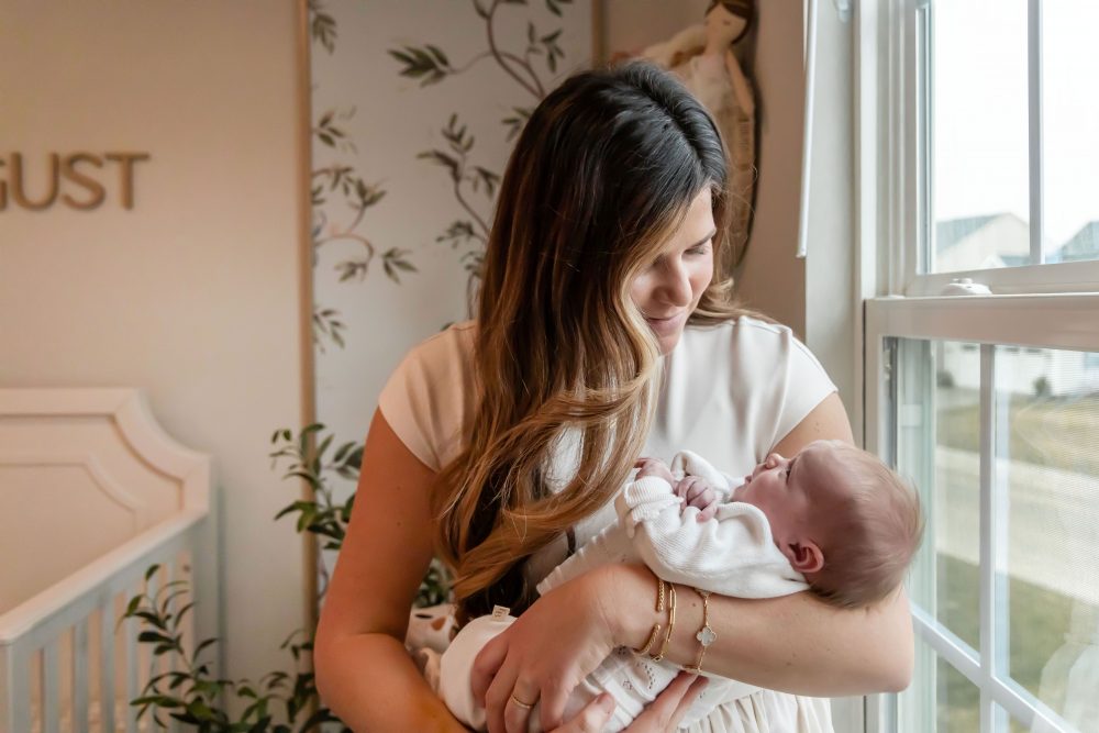 Mother and children standing together in a neutral-toned nursery, parents holding their newborn son while big sister cuddles with dad during an in-home newborn photography session in Cleveland.