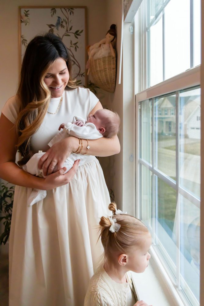 Mother and children standing together in a neutral-toned nursery, parents holding their newborn son while big sister cuddles with dad during an in-home newborn photography session in Cleveland.