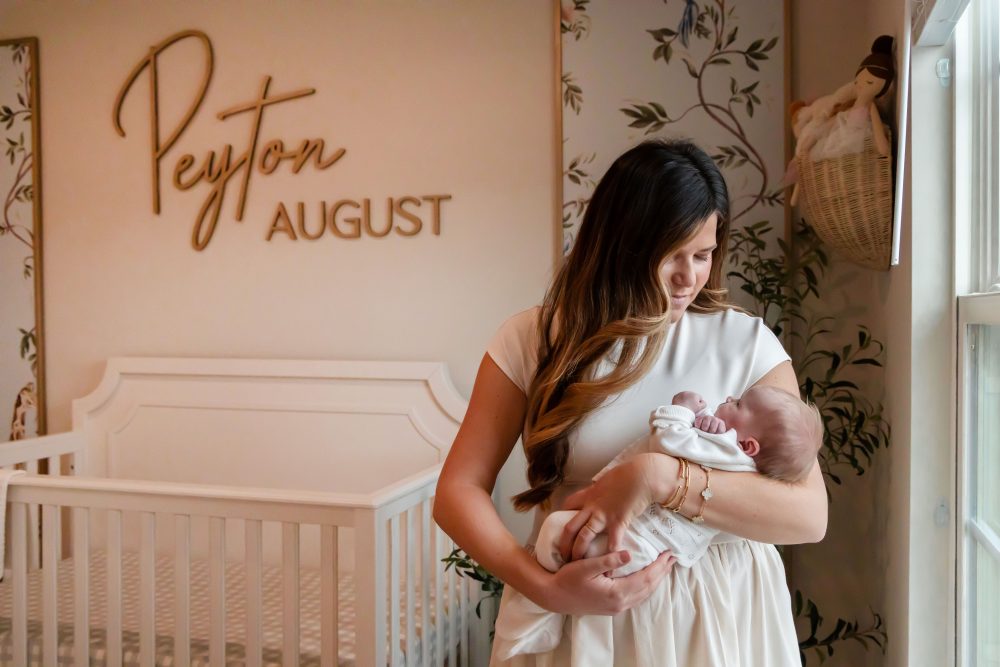 Mother and children standing together in a neutral-toned nursery, parents holding their newborn son while big sister cuddles with dad during an in-home newborn photography session in Cleveland.