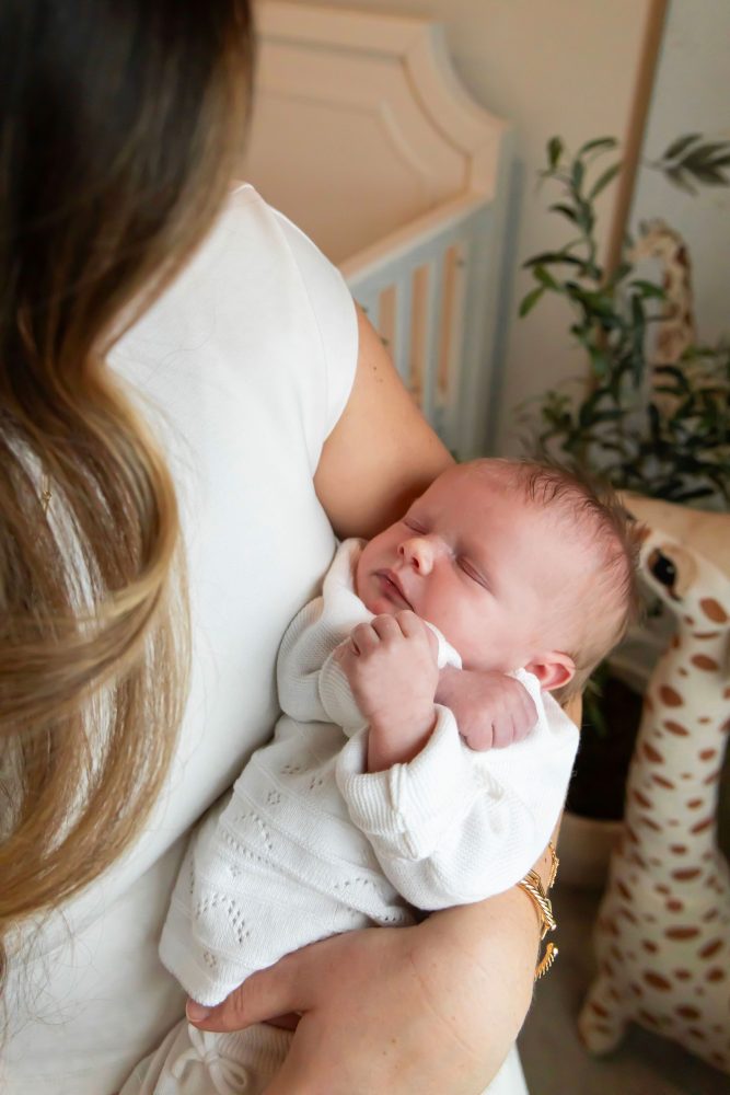Mother and children standing together in a neutral-toned nursery, parents holding their newborn son while big sister cuddles with dad during an in-home newborn photography session in Cleveland.