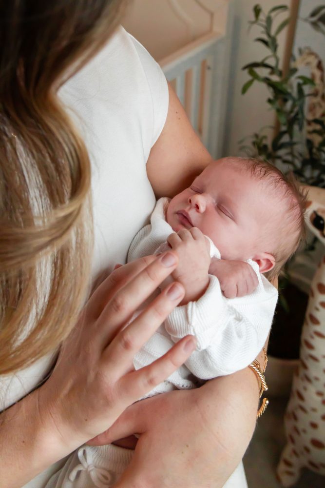 Mother and children standing together in a neutral-toned nursery, parents holding their newborn son while big sister cuddles with dad during an in-home newborn photography session in Cleveland.