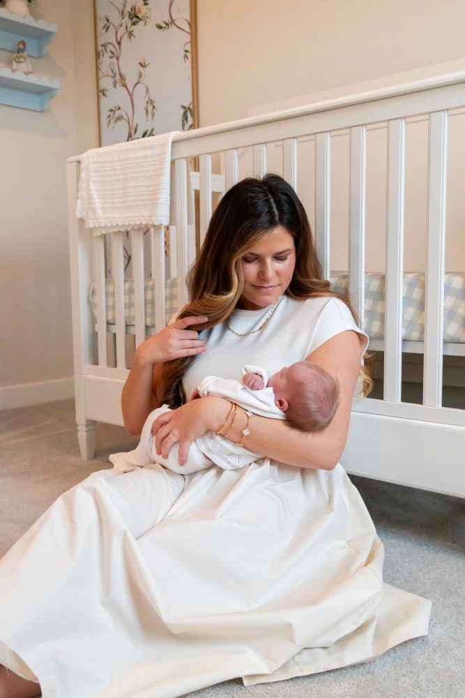 Parents sitting on the nursery floor with their newborn baby boy while big sister gently reaches toward her new sibling beside a white crib and custom nursery decor.
