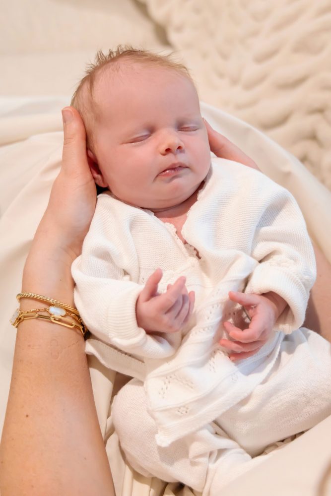 Lifestyle family portrait on a bed featuring newborn baby in the foreground with toddler smiling softly in the background during a cozy in-home newborn session.