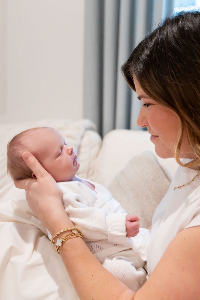 Lifestyle family portrait on a bed featuring newborn baby in the foreground with toddler smiling softly in the background during a cozy in-home newborn session.