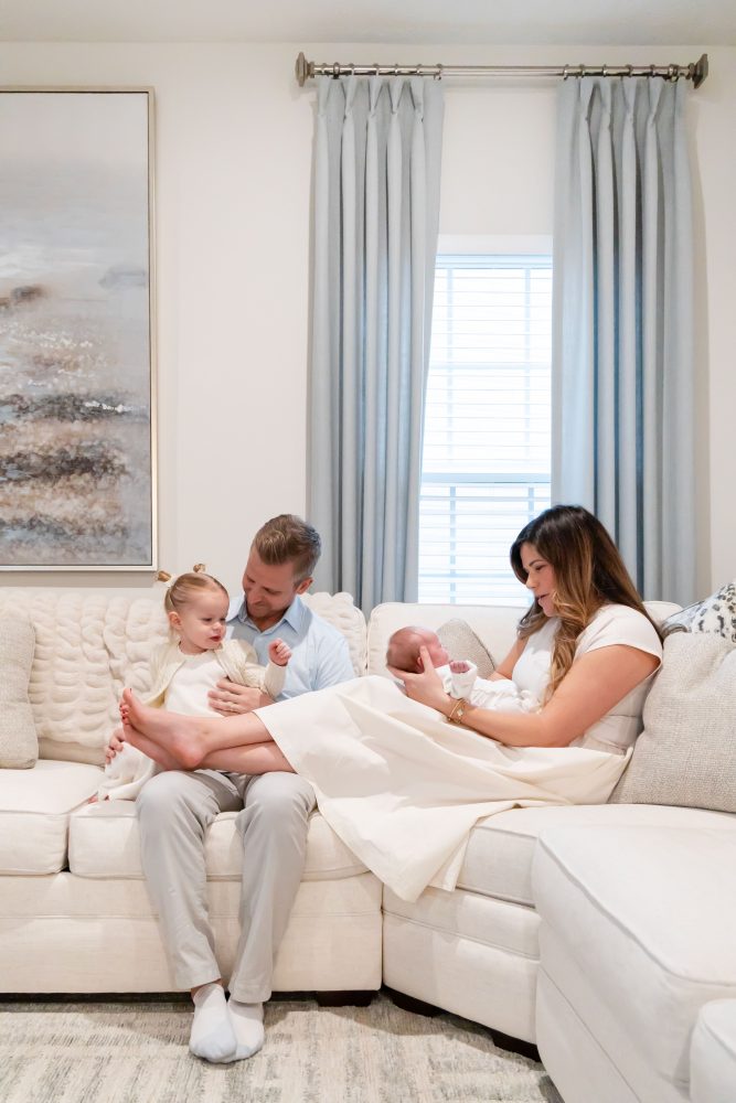 Lifestyle family portrait on a bed featuring newborn baby in the foreground with toddler smiling softly in the background during a cozy in-home newborn session.