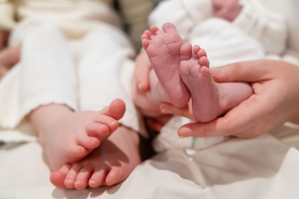 Lifestyle family portrait on a bed featuring newborn baby in the foreground with toddler smiling softly in the background during a cozy in-home newborn session.