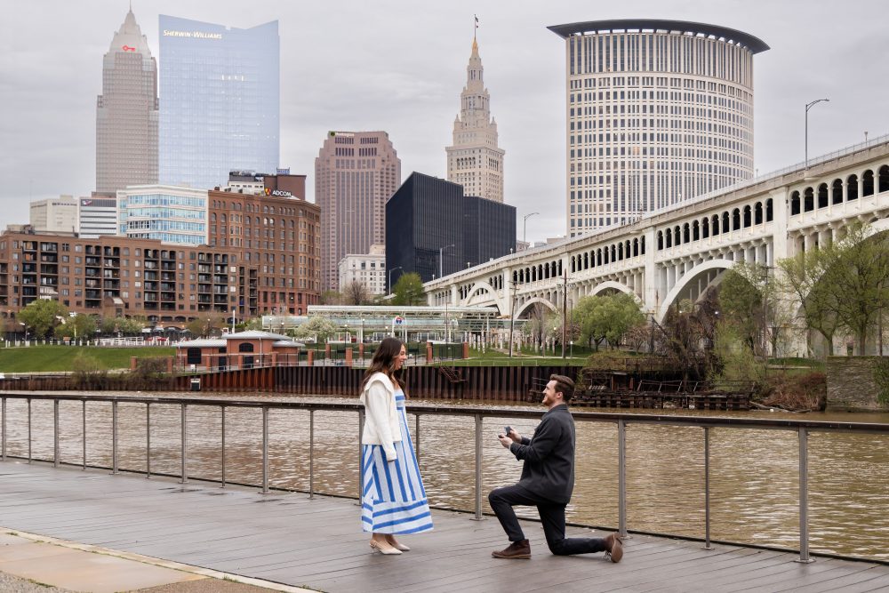 Couple celebrating a surprise proposal on a downtown Cleveland waterfront boardwalk with the Cleveland skyline in the background
