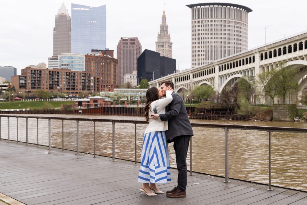 Couple celebrating a surprise proposal on a downtown Cleveland waterfront boardwalk with the Cleveland skyline in the background