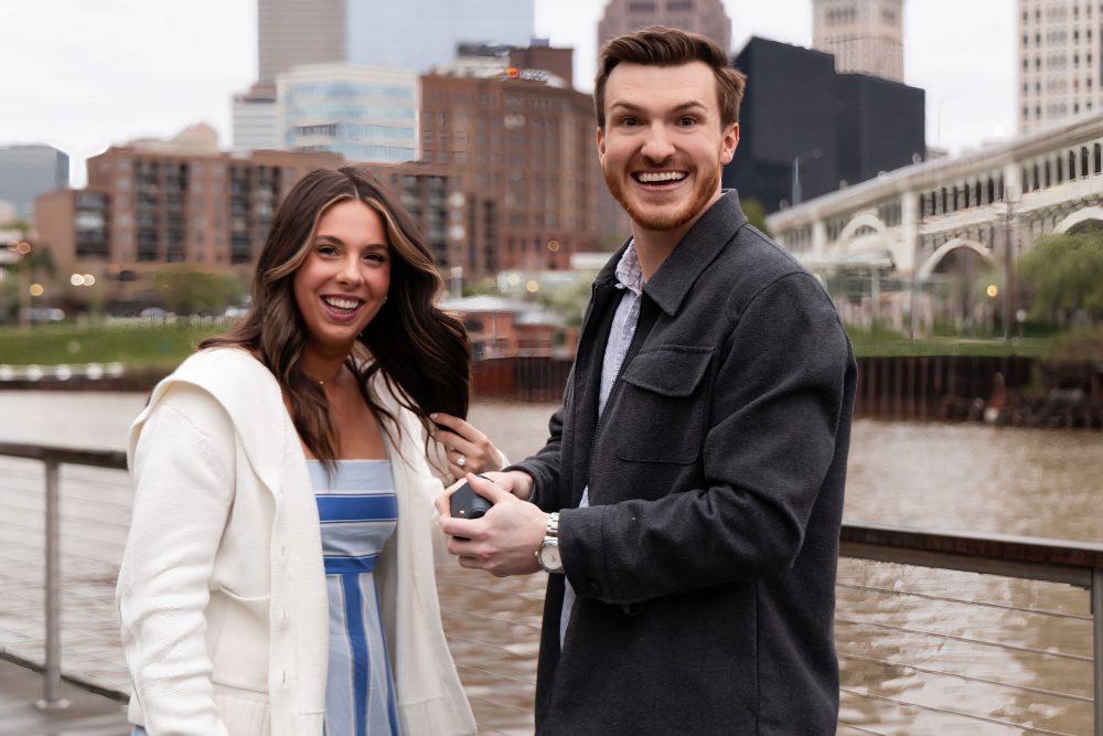 Romantic engagement portrait of newly engaged couple hugging along the Cleveland waterfront skyline