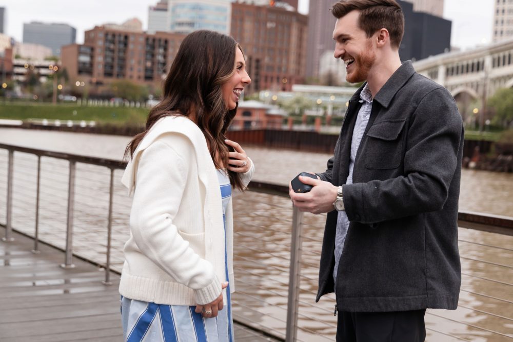 Romantic engagement portrait of newly engaged couple hugging along the Cleveland waterfront skyline