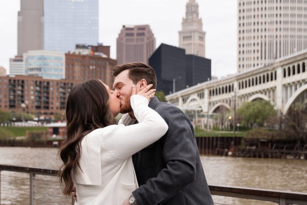 Romantic engagement portrait of newly engaged couple hugging along the Cleveland waterfront skyline