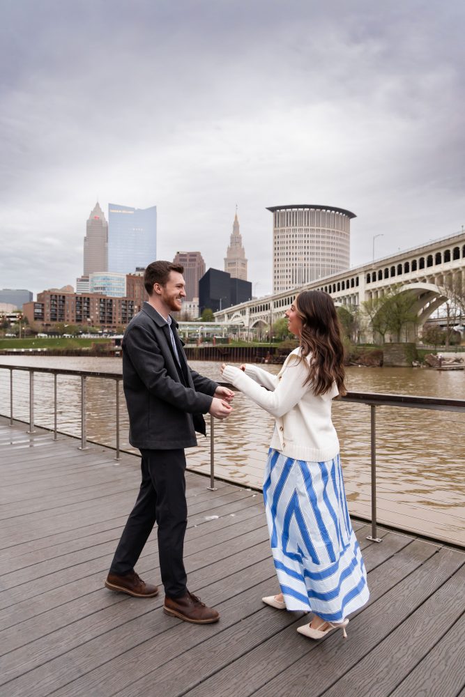 Romantic engagement portrait of newly engaged couple hugging along the Cleveland waterfront skyline