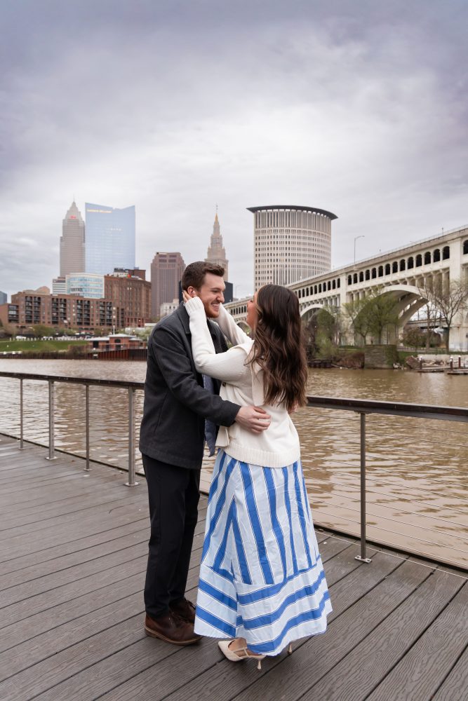 Romantic engagement portrait of newly engaged couple hugging along the Cleveland waterfront skyline