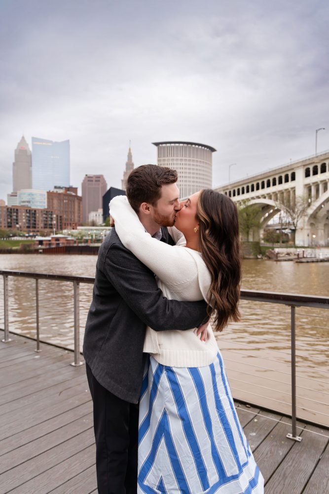 Romantic engagement portrait of newly engaged couple hugging along the Cleveland waterfront skyline