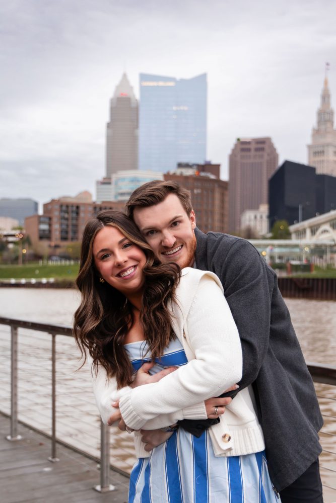 Romantic engagement portrait of newly engaged couple hugging along the Cleveland waterfront skyline