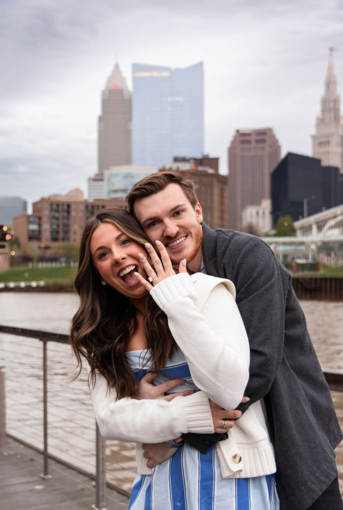 Romantic engagement portrait of newly engaged couple hugging along the Cleveland waterfront skyline