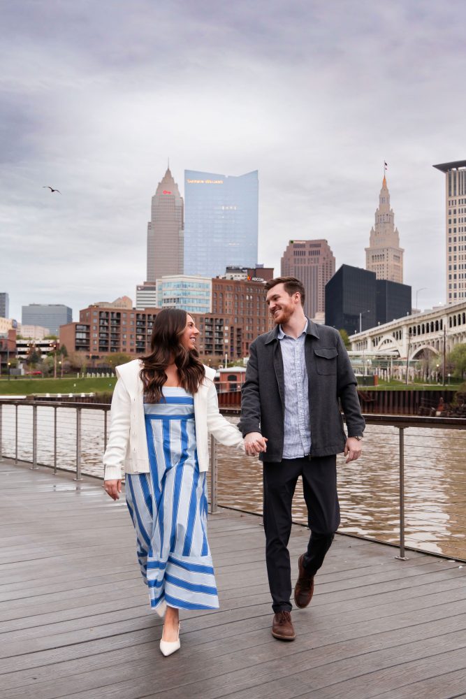 Couple celebrating a surprise proposal on a downtown Cleveland waterfront boardwalk with the Cleveland skyline in the background