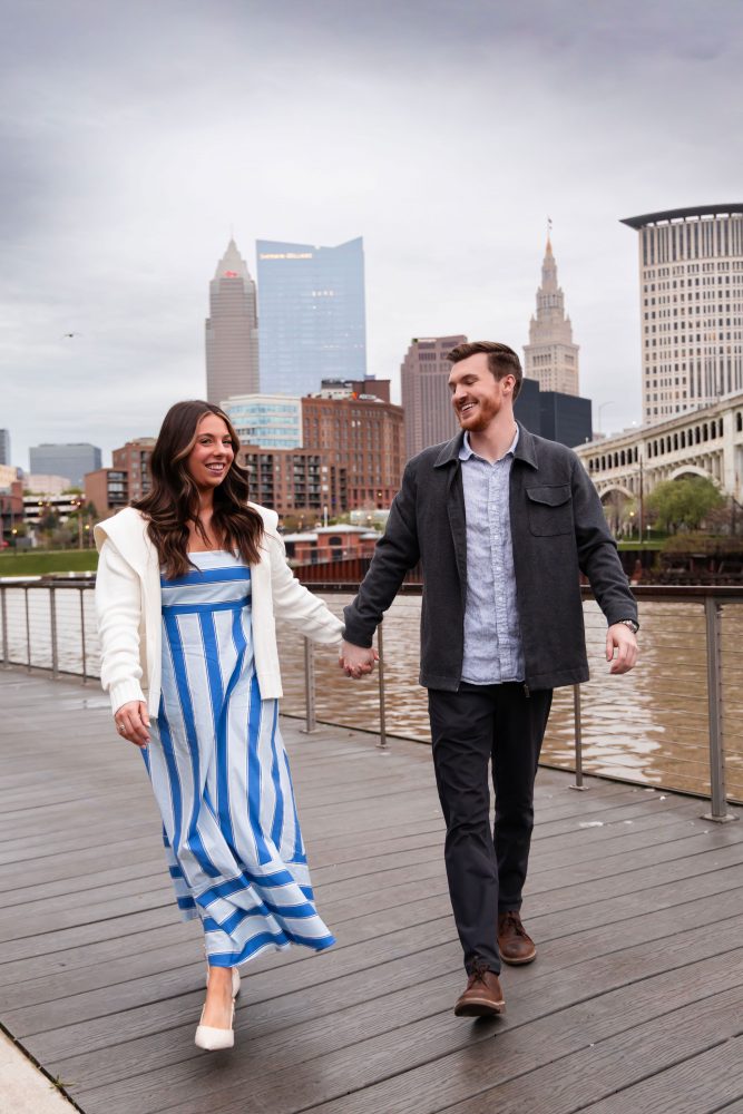 Couple celebrating a surprise proposal on a downtown Cleveland waterfront boardwalk with the Cleveland skyline in the background