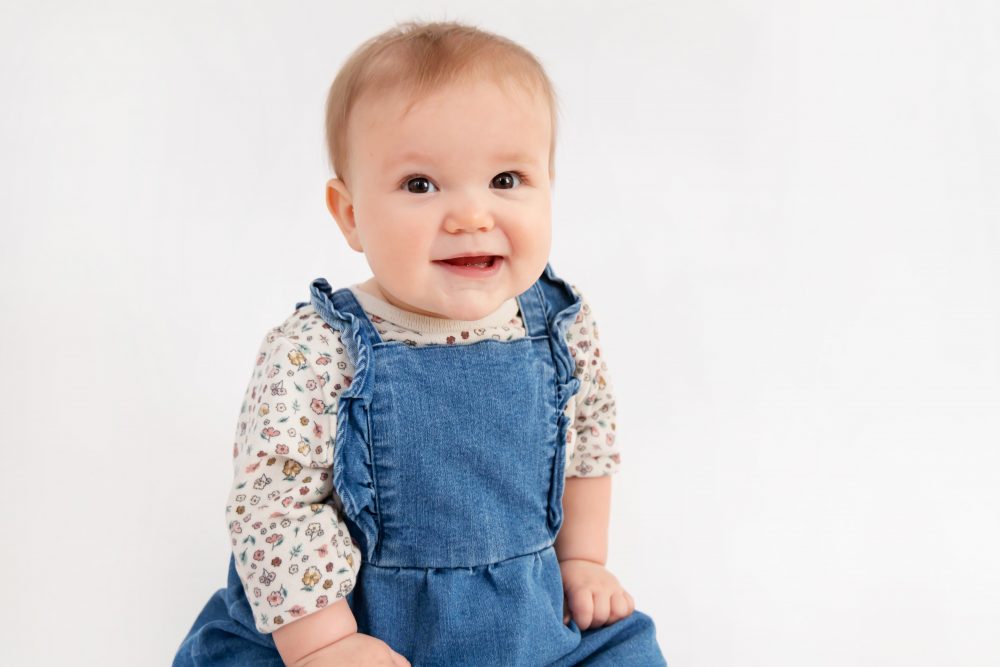 Older brother sitting with baby sister in a studio, smiling and cuddling, neutral white background family portrait